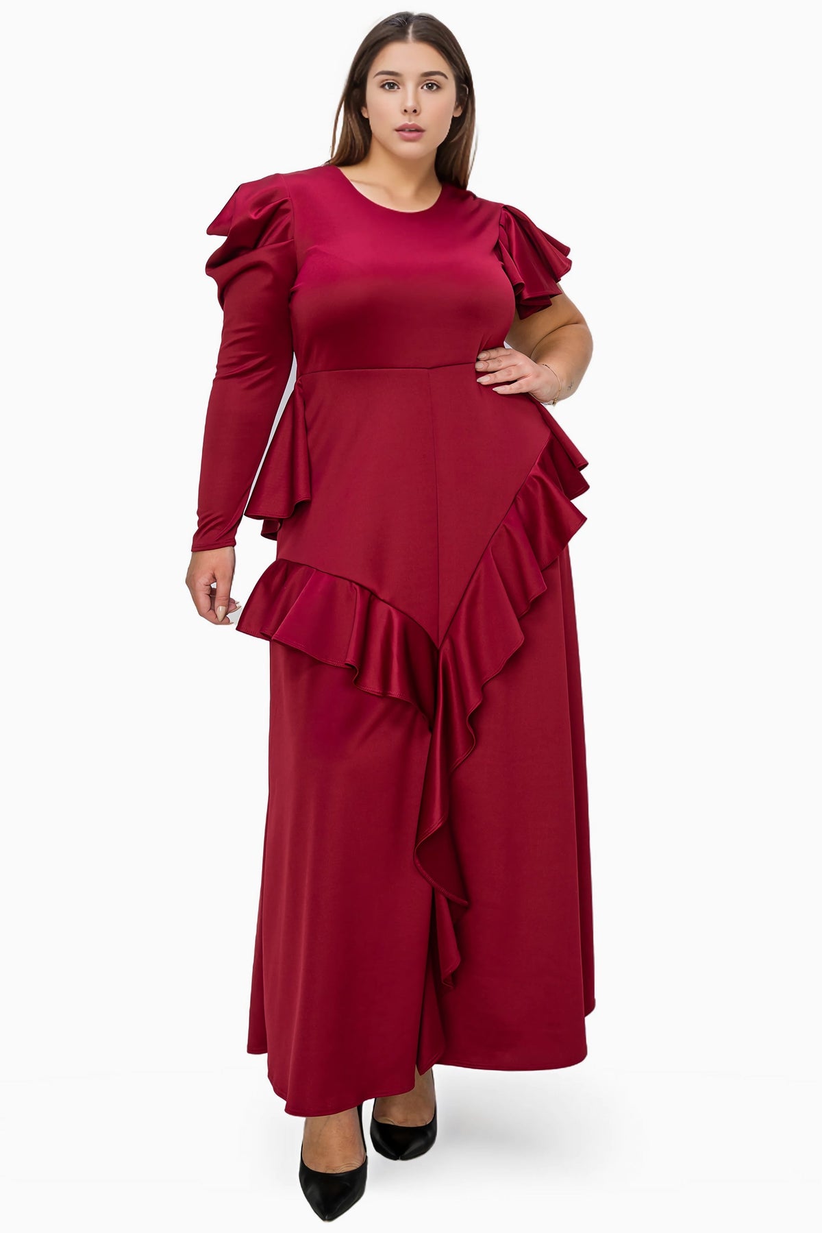 A woman modeling a long-sleeve maxi dress in deep burgundy with dramatic ruffle details on the shoulders and a layered asymmetrical hem, paired with black pointed-toe heels against a plain white studio background.
