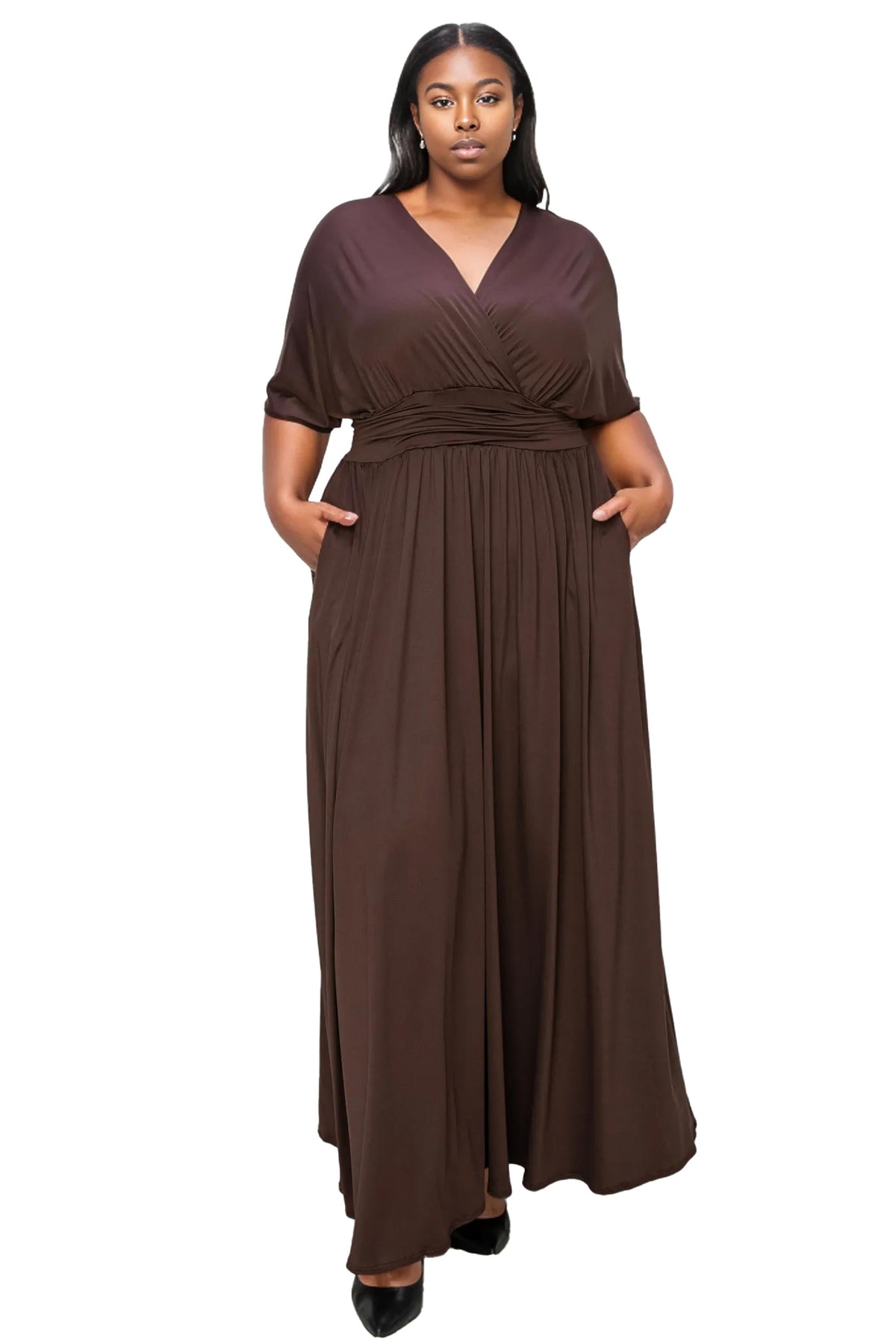 A woman modeling a dark brown maxi dress with short sleeves, a V-neckline, and side pockets, standing against a plain white background.