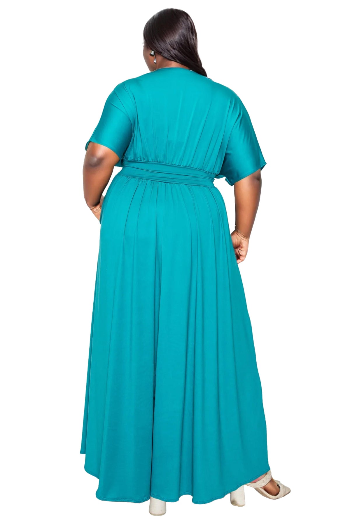 A woman viewed from the back wearing a flowing teal maxi dress with short sleeves and a matching waist tie, photographed against a plain white background.