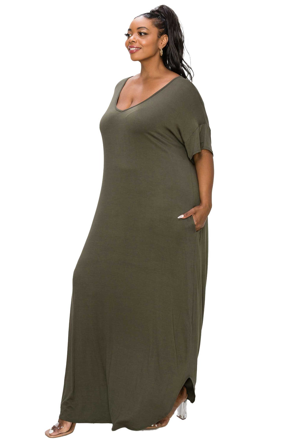 A woman modeling a loose, olive green maxi dress with short sleeves and a V-neckline, standing against a plain white background.