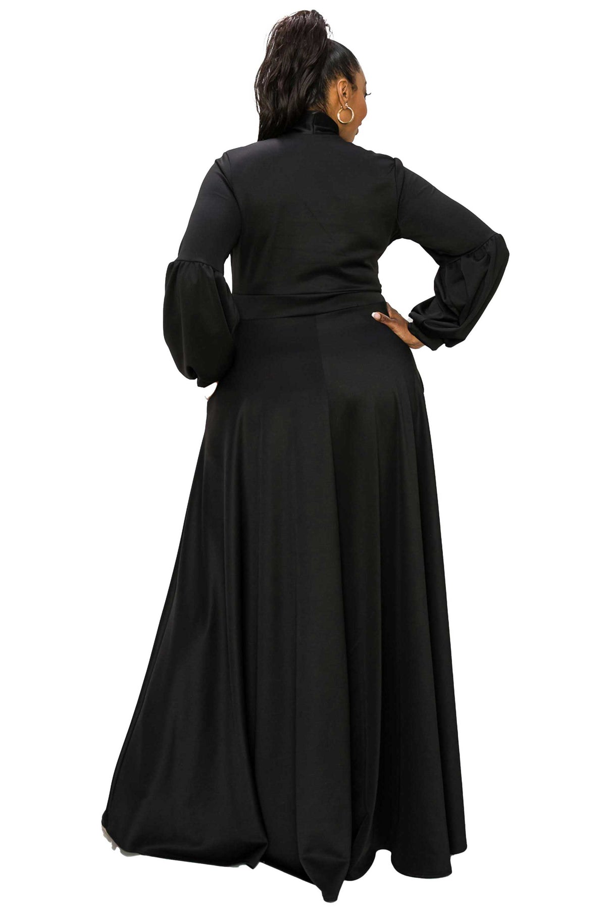 A woman modeling a long black maxi dress from the back, featuring a high neck, long sleeves with gathered cuffs, and a flowing skirt, set against a plain white background.