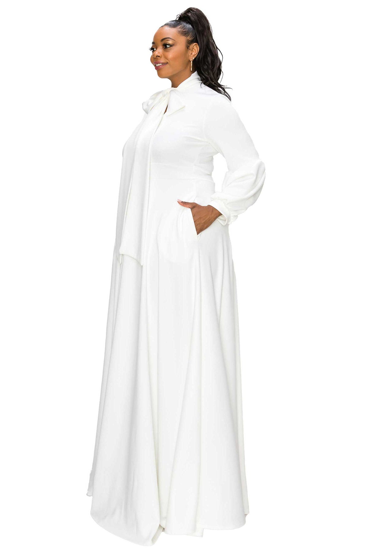 A woman modeling a long white maxi dress with a high collar, wide sleeves, and side pockets, shown from a side profile against a plain white background.