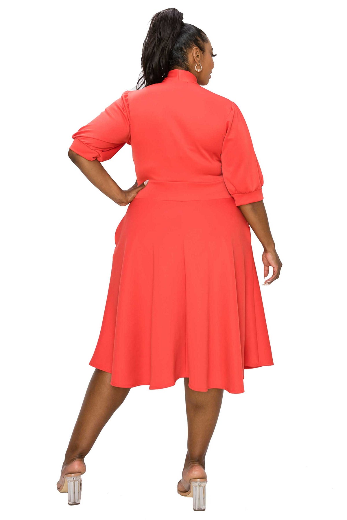 A woman modeling a coral red midi shirt dress from the back, featuring three-quarter sleeves, a high collar, and a flared skirt, set against a plain white background.