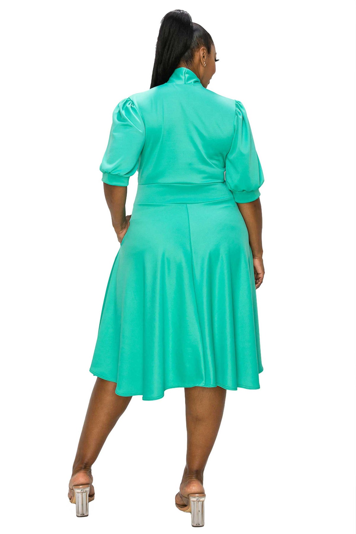 A woman shown from the back wearing a bright turquoise green midi dress with puff sleeves and a high mock neck, paired with clear high-heeled sandals, against a plain white background.