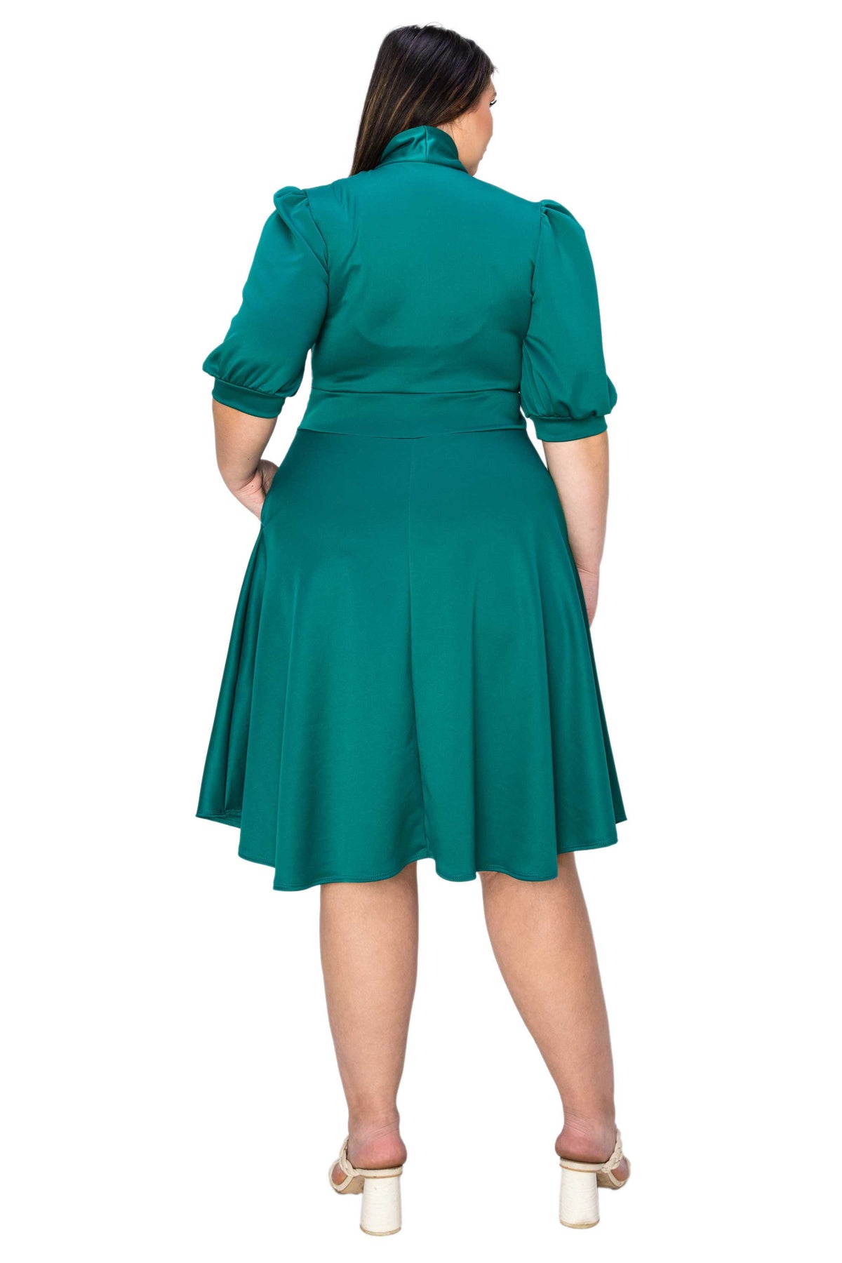 A woman shown from the back wearing a teal green midi dress with puff sleeves and a pleated skirt, paired with white block-heel sandals, against a plain white background.