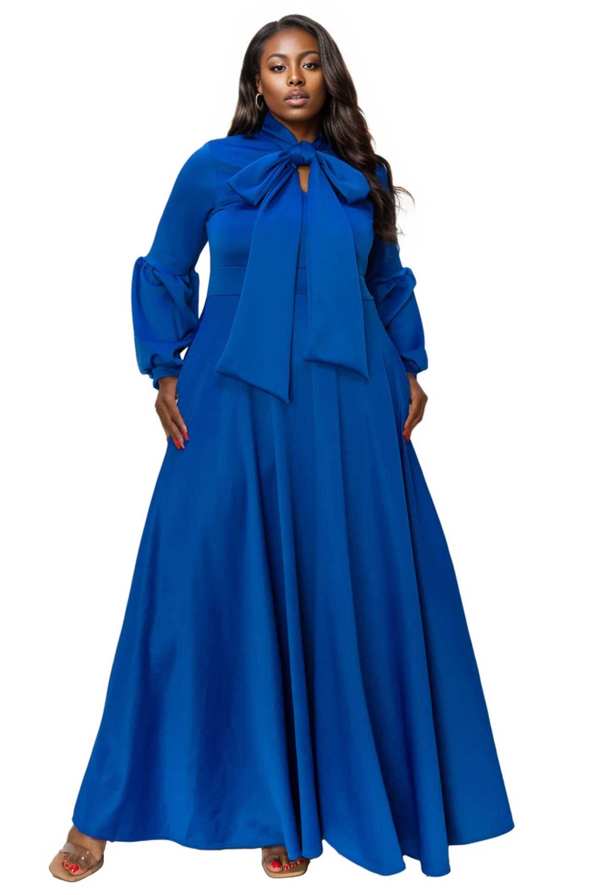 A woman modeling a long-sleeved royal blue maxi dress with a large bow at the collar, photographed against a plain white background.