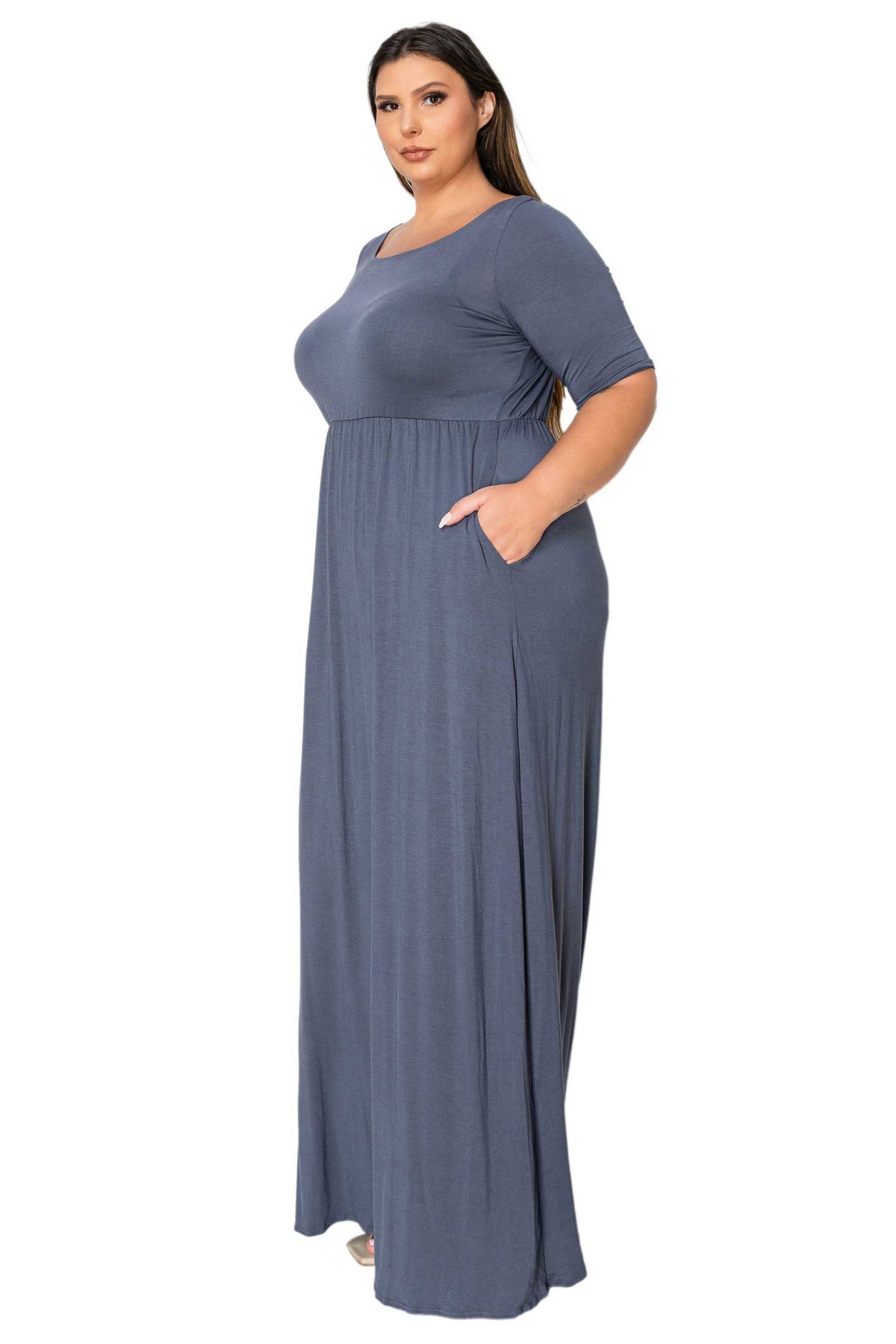 A woman modeling a floor-length, short-sleeve dress in a muted slate blue-gray color, standing against a plain white background.