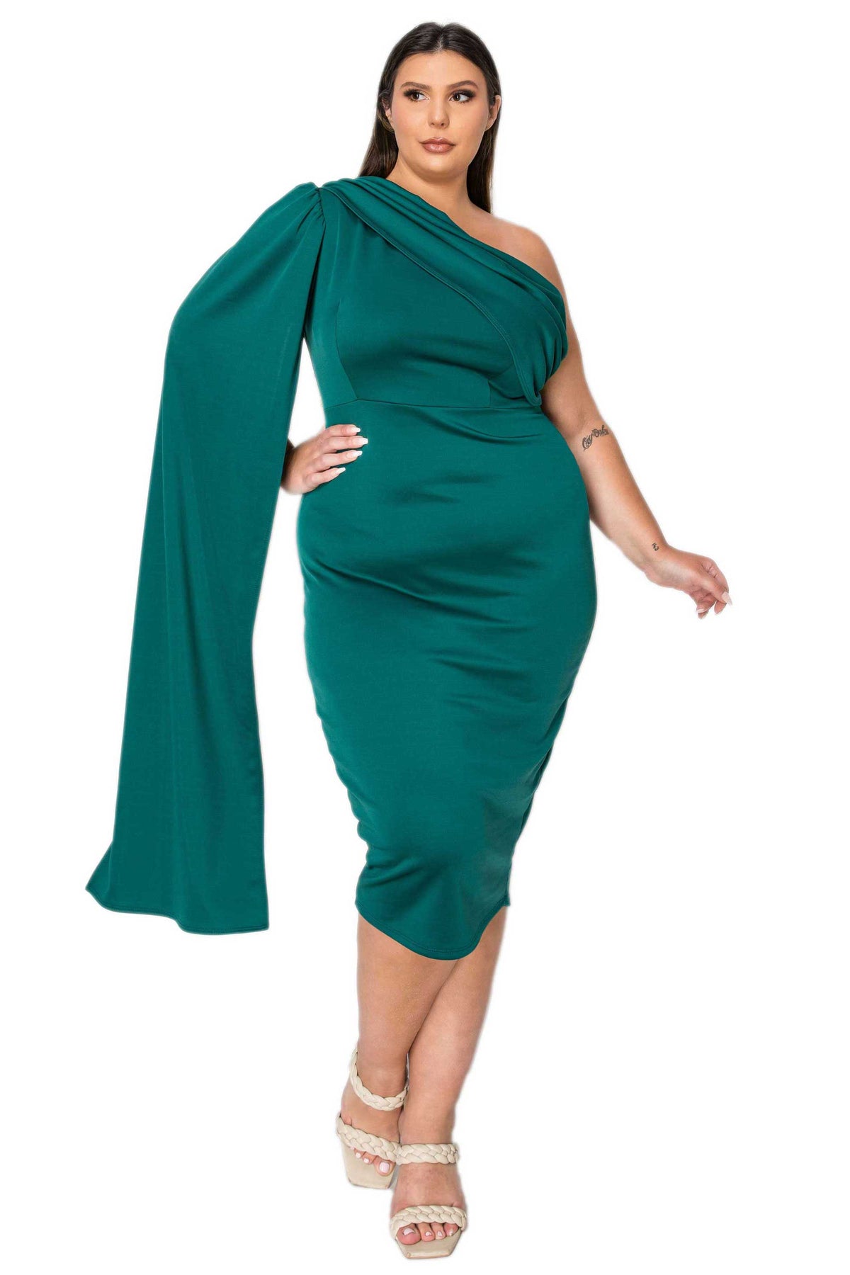 A woman modeling a one-shoulder emerald green midi dress with a dramatic draped cape sleeve, paired with beige platform sandals, against a plain white background.