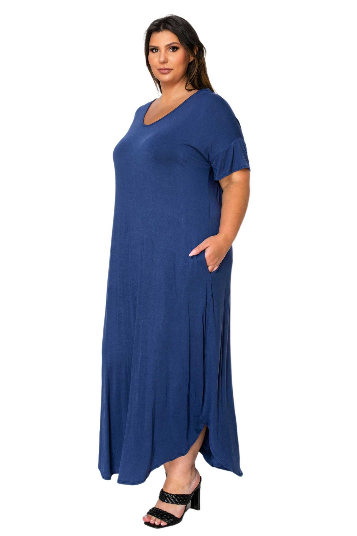 A woman modeling a loose-fitting, short-sleeve blue maxi dress with a V-neck and side pockets, paired with black heeled sandals, against a plain white background.