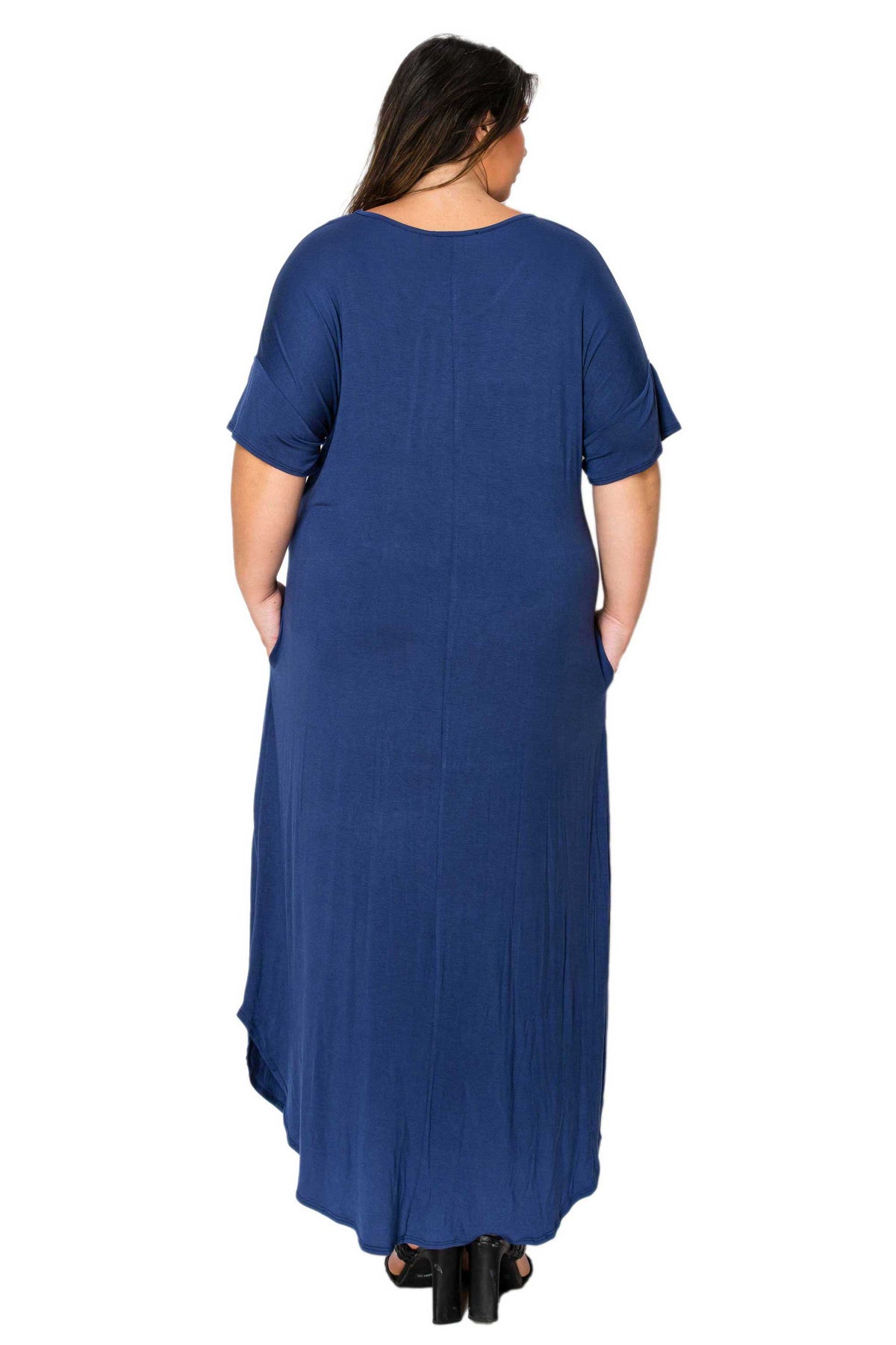 A woman viewed from the back wearing a loose, short-sleeve maxi dress in a medium-to-deep blue color, paired with black heels, against a plain white background.