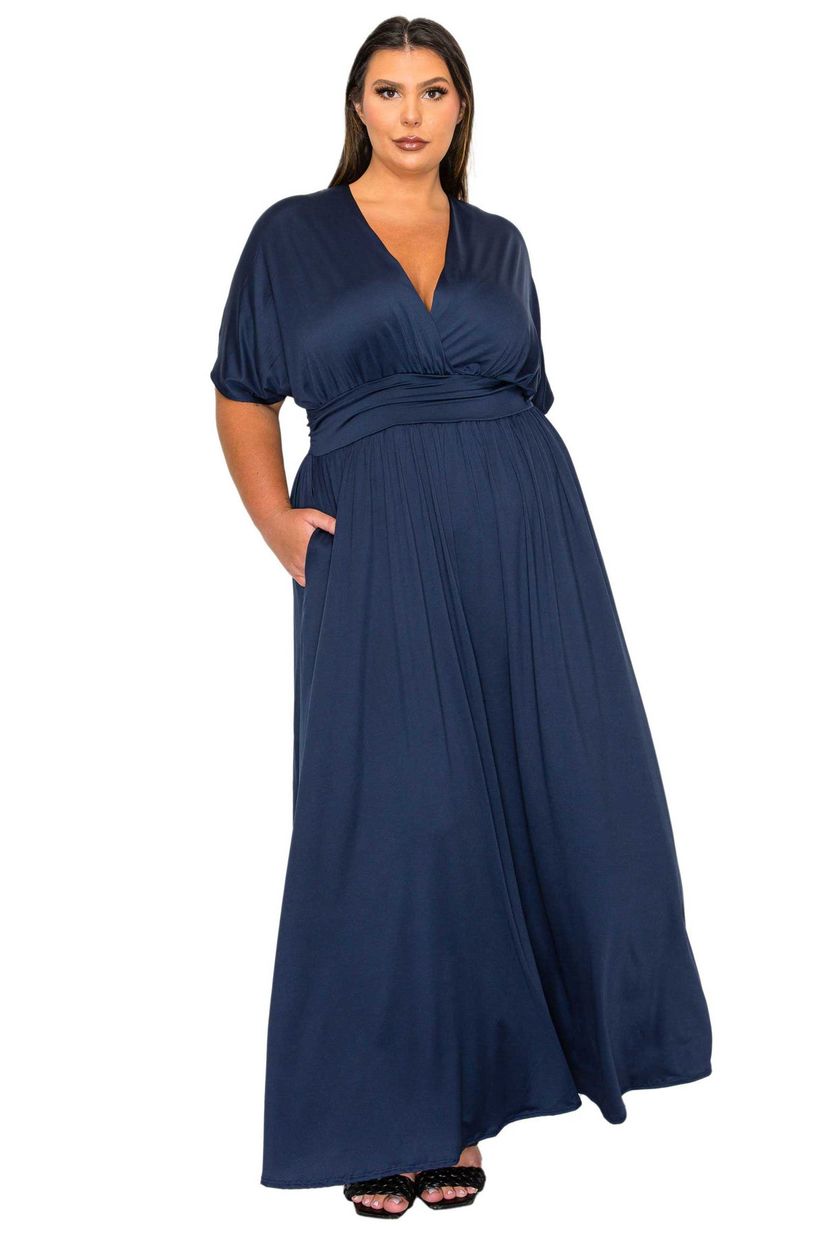 A woman modeling a navy blue maxi dress with short puff sleeves, a V-neckline, and side pockets, set against a plain white background.