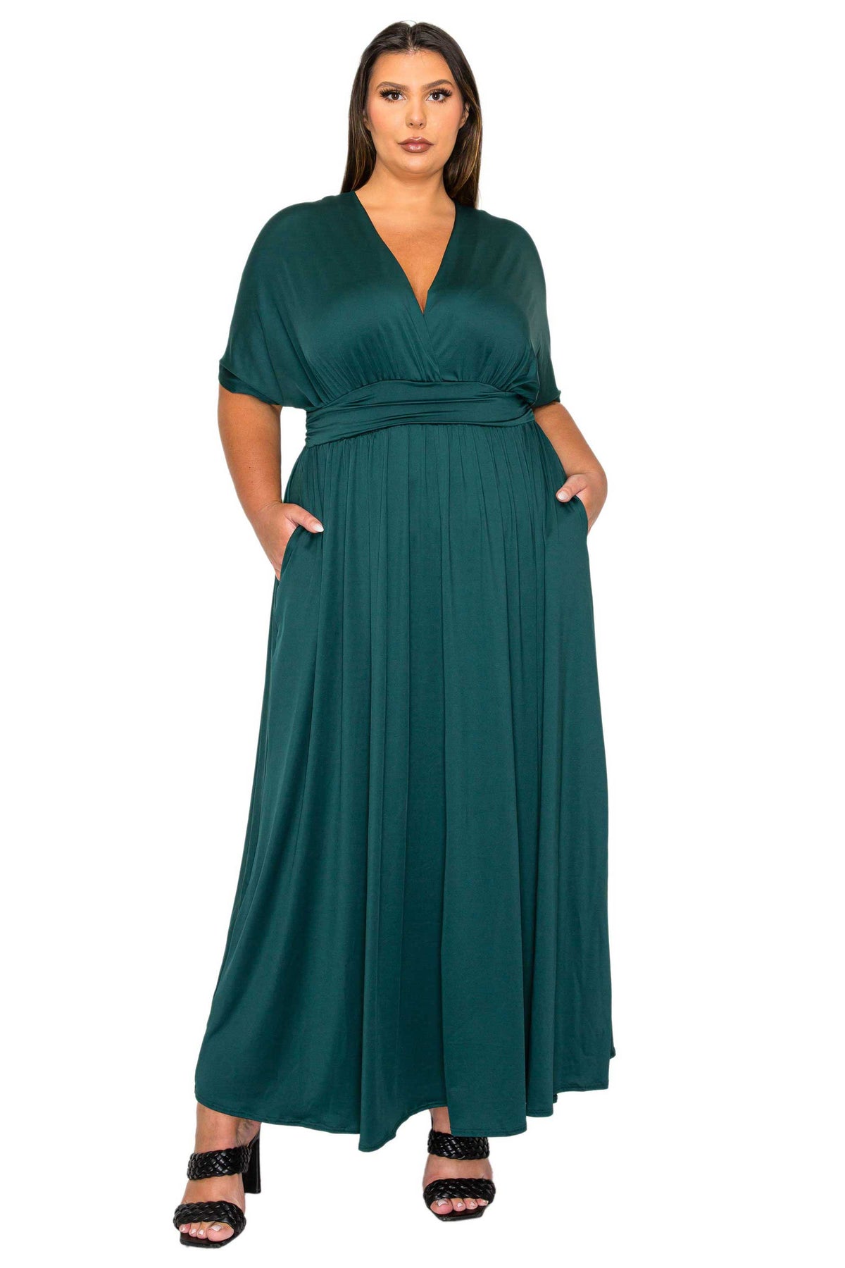 A woman modeling a dark teal green maxi dress with short flutter sleeves, a V-neckline, and side pockets, paired with black heeled sandals against a plain white background.