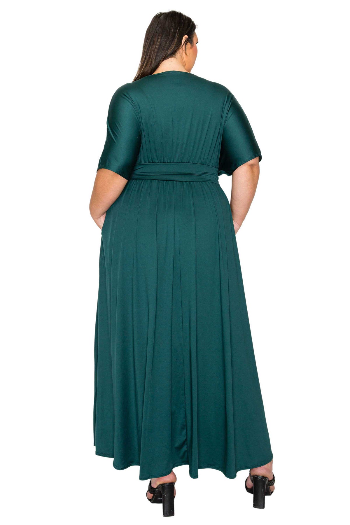 A woman viewed from the back wearing a dark teal green short-sleeve maxi dress with a matching waist tie, paired with black block-heeled sandals, against a plain white background.