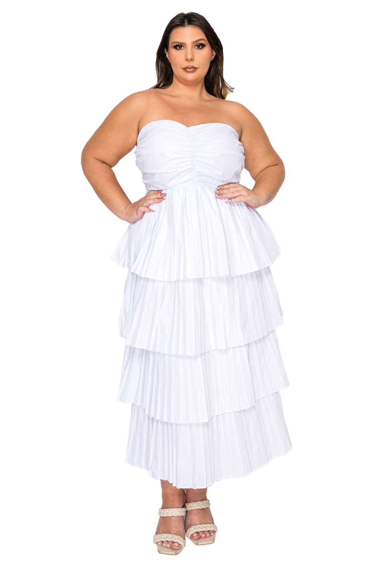 A woman modeling a strapless white tiered maxi dress with a ruched sweetheart bodice and pleated layered skirt, paired with beige platform sandals, against a plain white background.