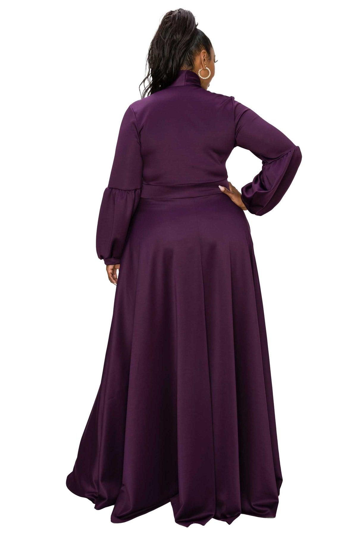 A woman shown from the back wearing a long-sleeve, high-neck, floor-length purple dress with a matching belt and flared skirt, photographed against a plain white background.