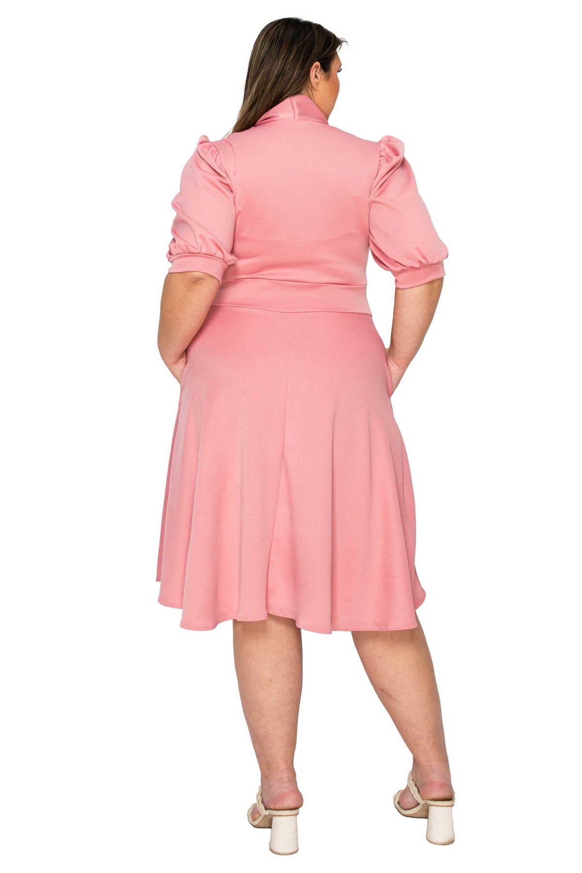 A woman viewed from the back wearing a pink short-sleeve midi dress with puffed sleeves and a flared skirt, paired with white heeled sandals, against a plain white background.