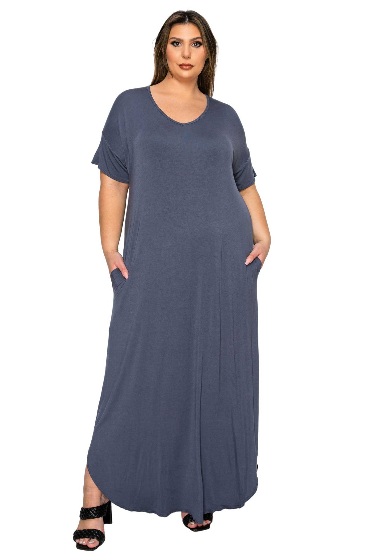 A woman modeling a slate blue-gray short-sleeve maxi dress with side pockets, paired with black heeled sandals, against a plain white background.