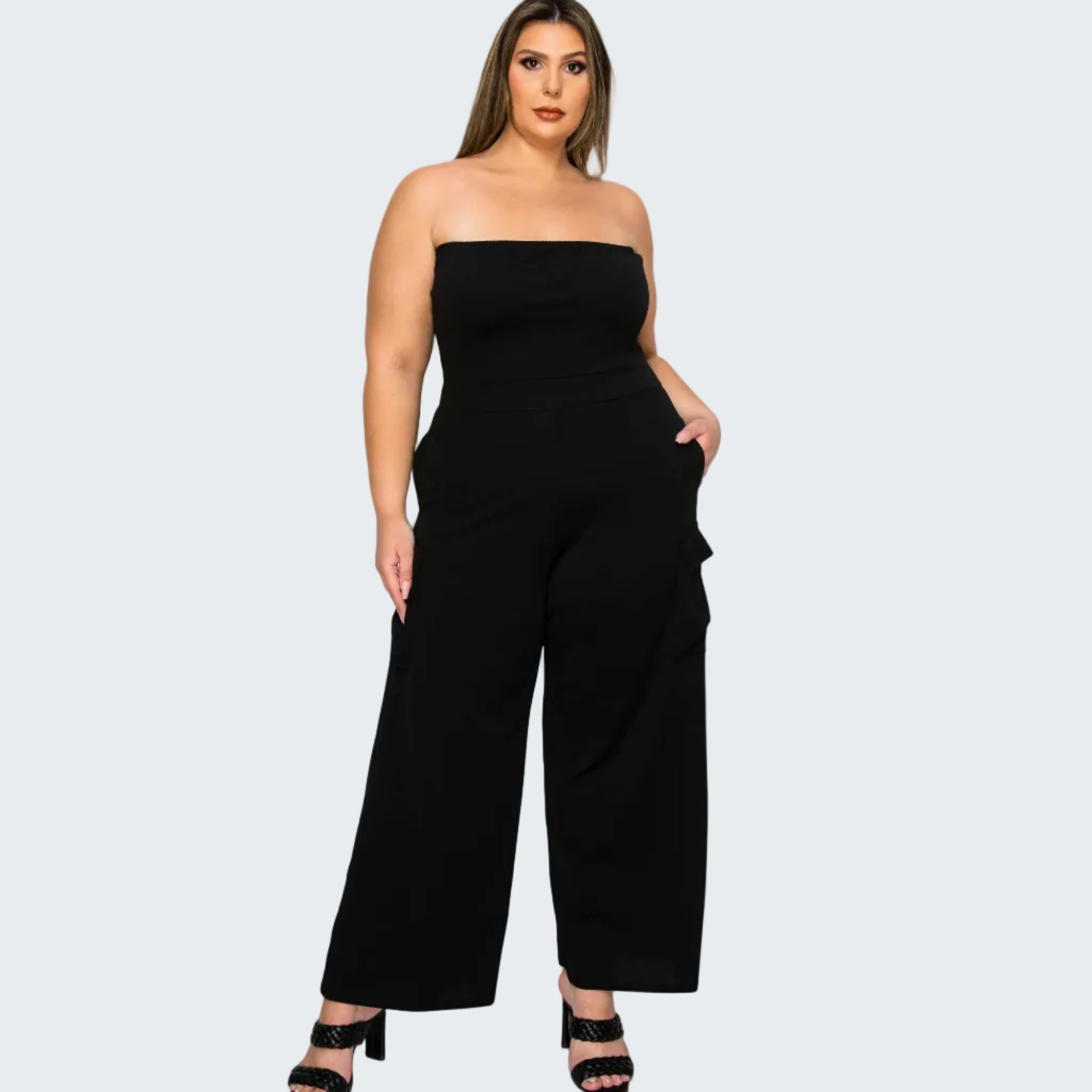 A woman modeling a black strapless wide-leg jumpsuit with side cargo pockets, paired with black heeled sandals, against a plain white background.