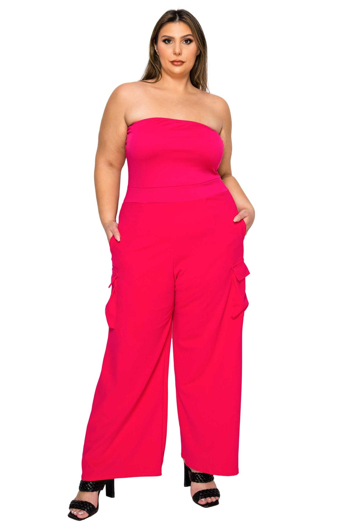 A woman modeling a bright hot pink strapless jumpsuit with wide legs and side cargo pockets, paired with black heeled sandals, against a plain white background.