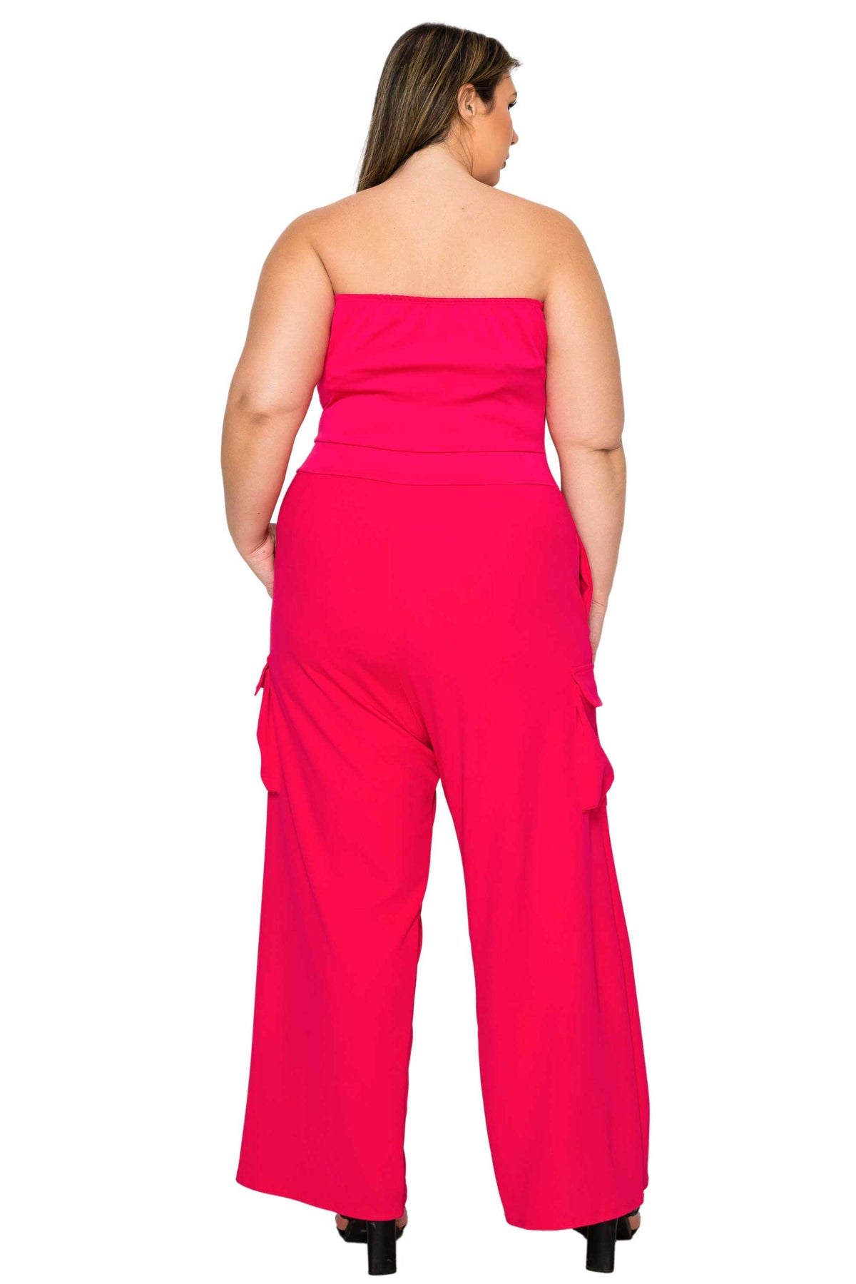 A woman shown from the back wearing a bright pink strapless jumpsuit with wide legs and side cargo pockets, photographed against a plain white background.