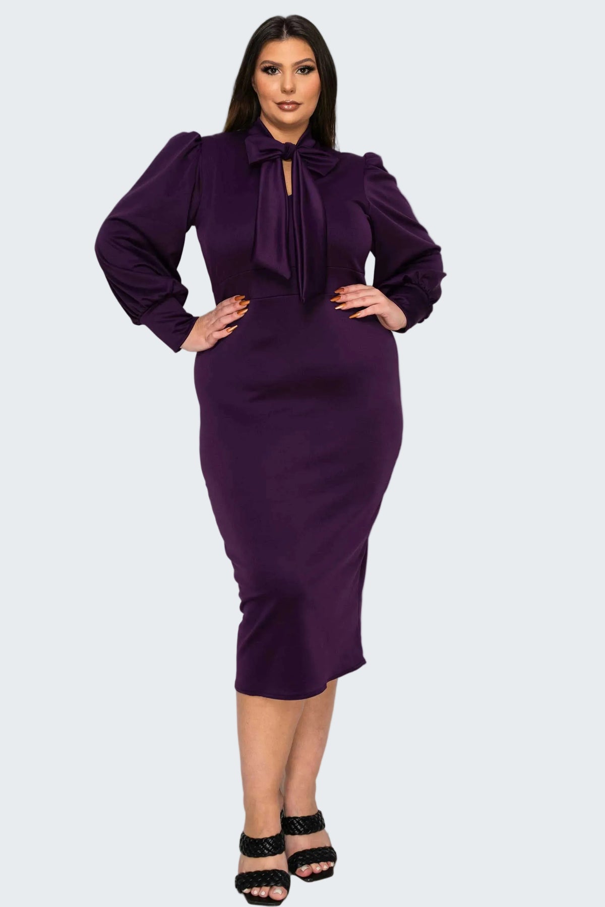 A woman modeling a fitted knee-length purple dress with long balloon sleeves, a large bow at the neckline, and a keyhole cutout, paired with black strappy heels against a plain white background.