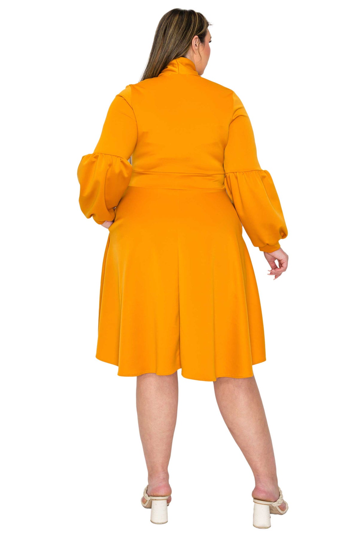 A woman viewed from the back wearing a bright orange-yellow long-sleeve dress with puffed balloon sleeves and a matching waist tie, paired with beige high-heeled sandals, against a plain white background.