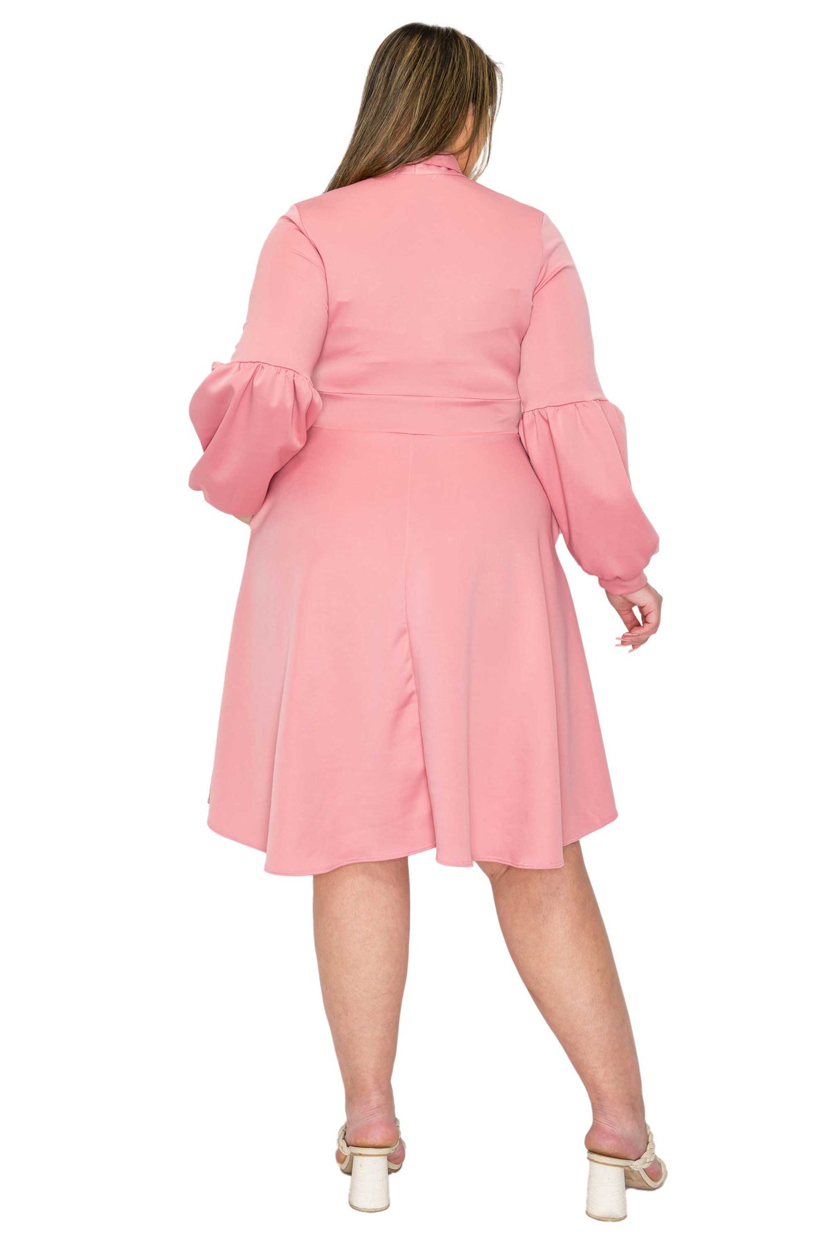 A woman shown from the back wearing a pink long-sleeve dress with puffed balloon sleeves and a flared skirt, paired with white block-heel sandals, against a plain white background.