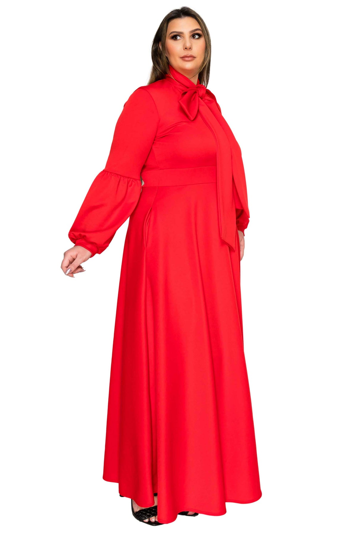 A woman modeling a bright red long-sleeve maxi dress with a high neck, bow detail at the collar, and a matching waist tie, set against a plain white background.