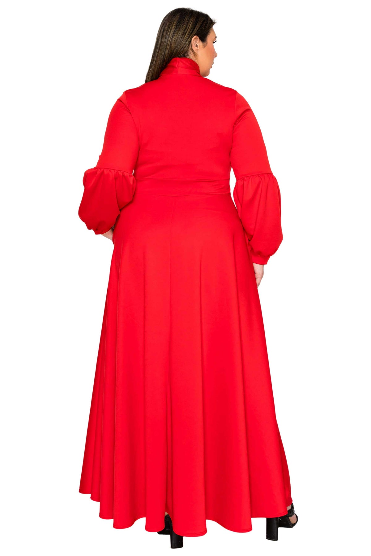 A woman viewed from the back wearing a bright red long-sleeve maxi dress with a high mock neck and voluminous puffed sleeves, paired with black heels against a plain white background.