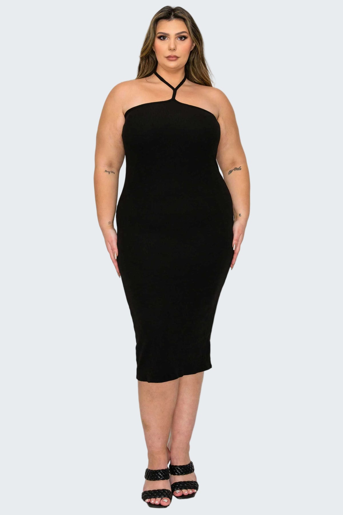 A woman modeling a black halter-neck midi dress with a bodycon fit, paired with black strappy high-heeled sandals, against a plain white background.