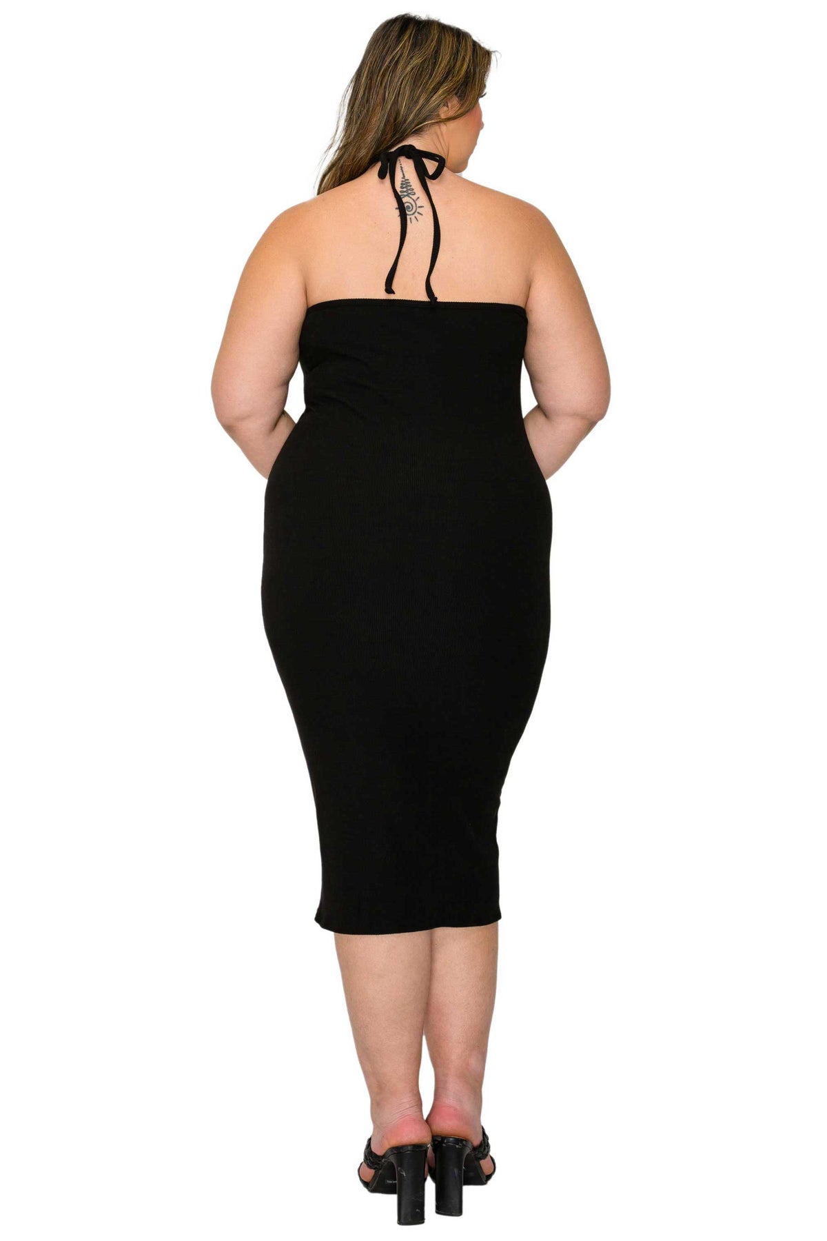 A woman viewed from the back wearing a strapless black bodycon midi dress with tie-back straps and black heeled sandals, against a plain white studio background.