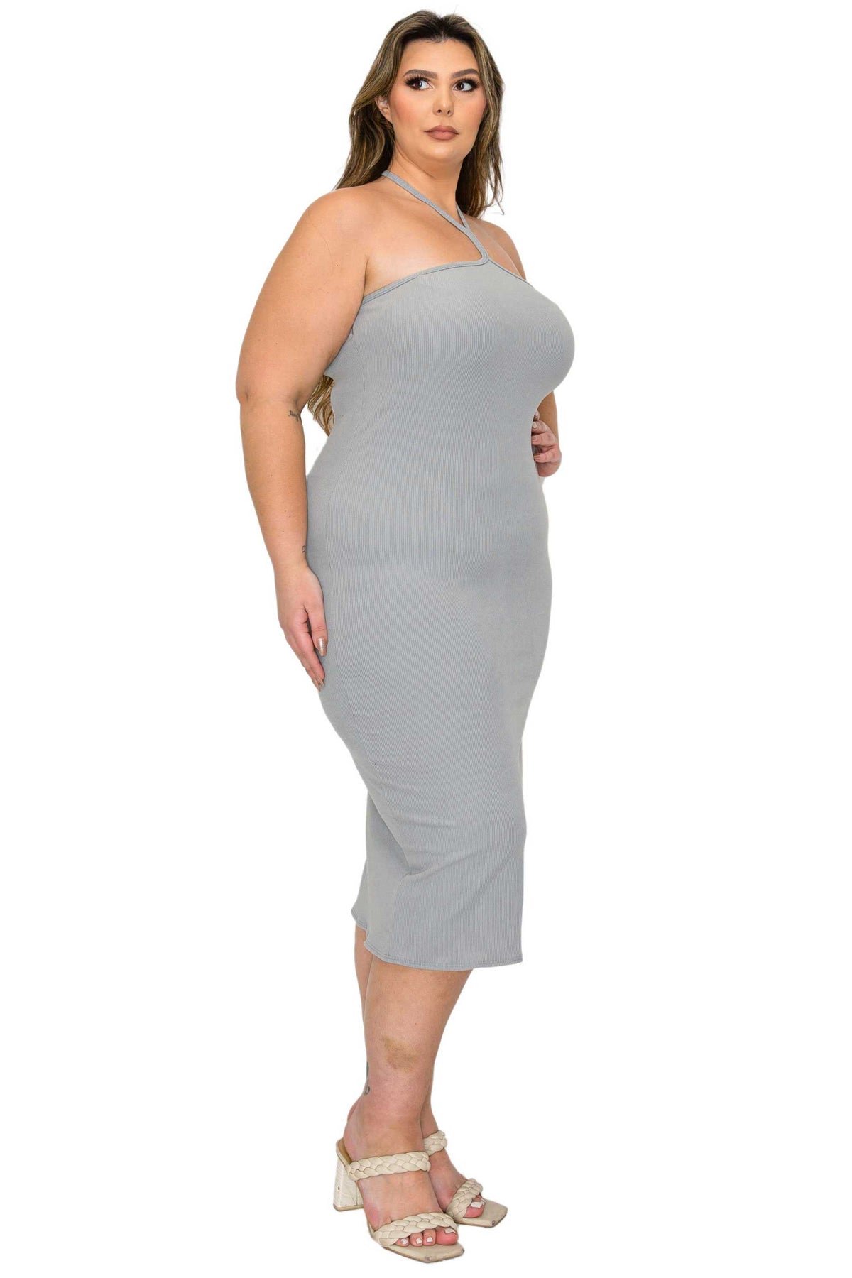 A woman modeling a light gray halter-neck midi dress with a bodycon fit, paired with beige heeled sandals, against a plain white background.