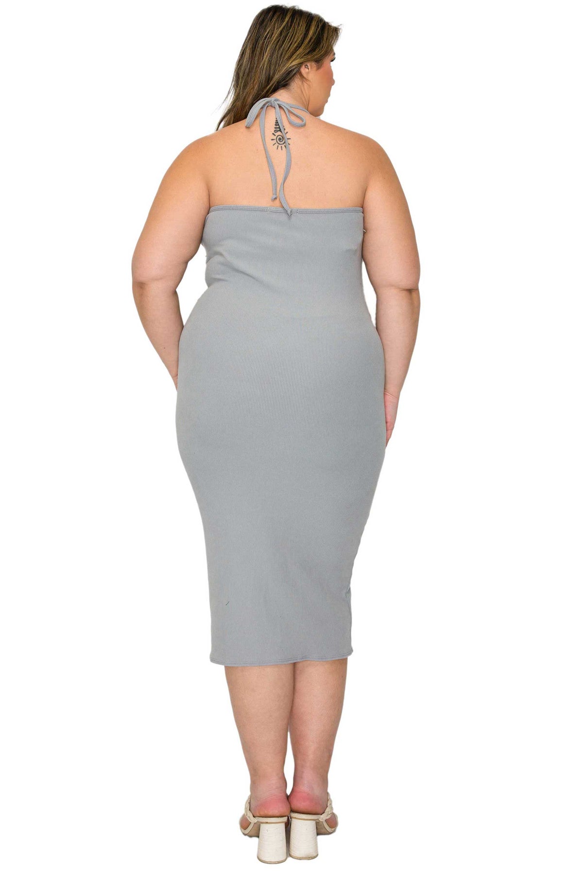 A woman shown from the back wearing a light gray halter midi dress with tie straps at the neckline, paired with white block-heel sandals, against a plain white background.