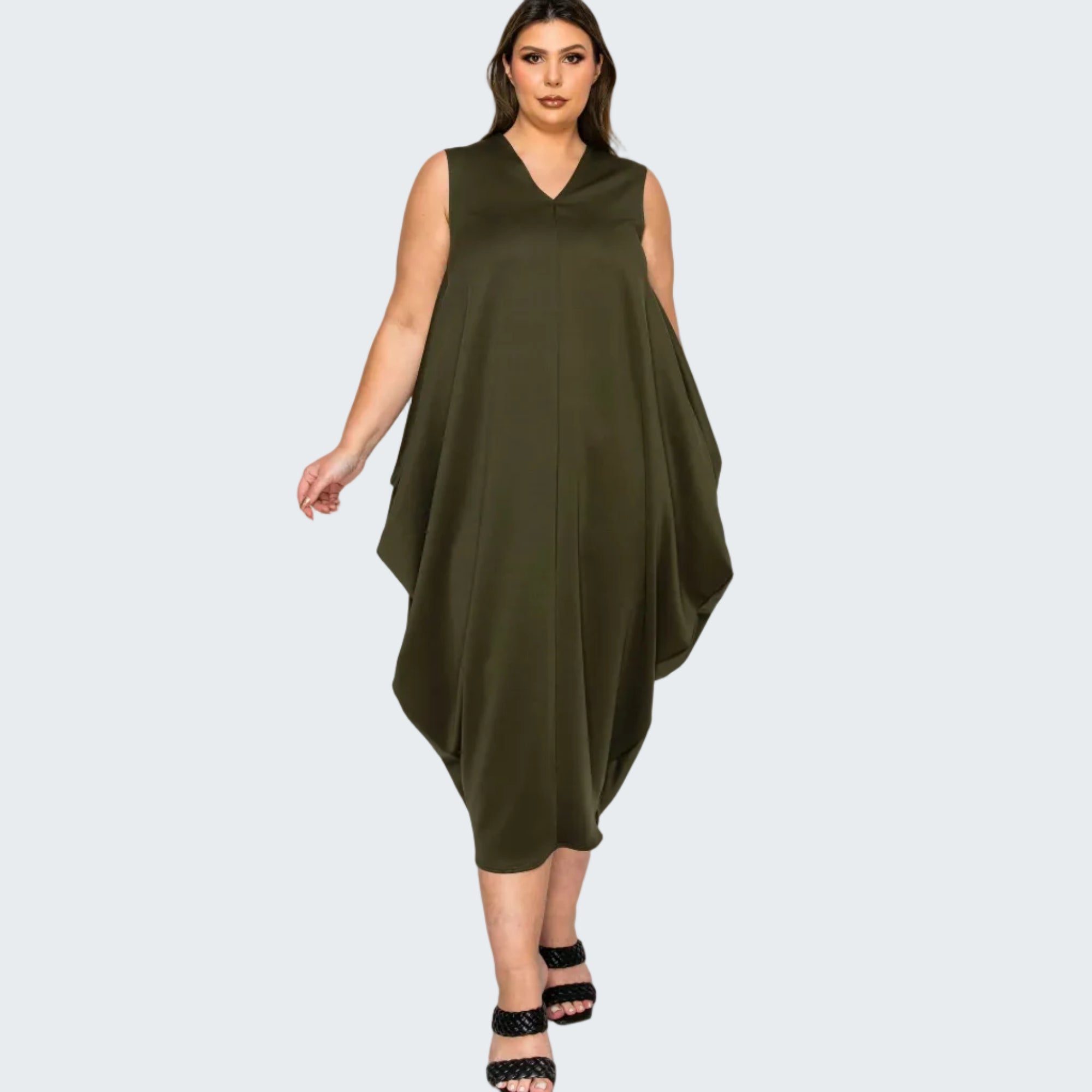 A woman modeling a sleeveless olive green V-neck dress with a draped, asymmetrical hem, paired with black strappy heels, against a plain white background.