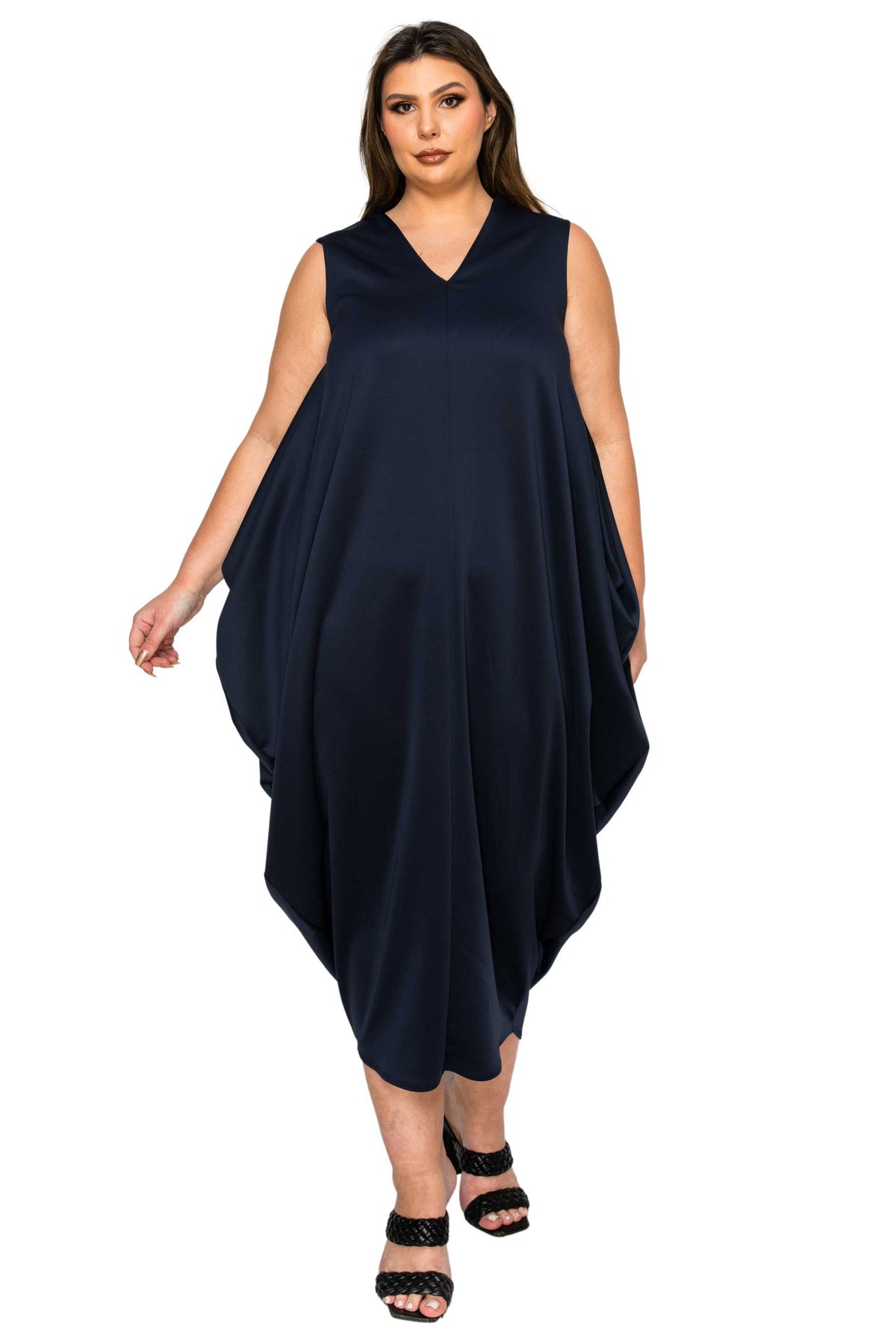 A woman modeling a sleeveless navy blue maxi dress with a V-neckline and draped, flowy silhouette, paired with black strappy sandals against a plain white background.