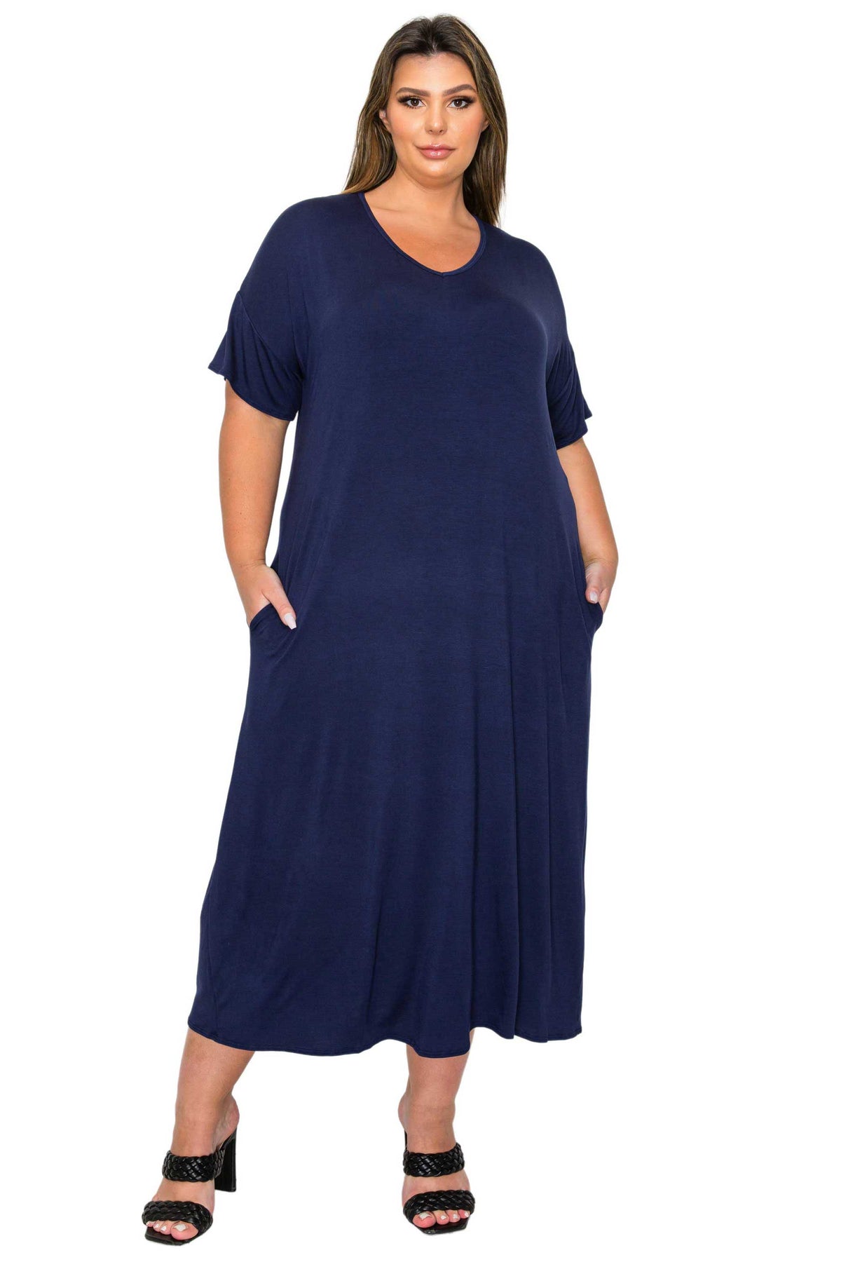 A woman modeling a navy blue short-sleeve maxi dress with side pockets, paired with black heeled sandals, against a plain white background.