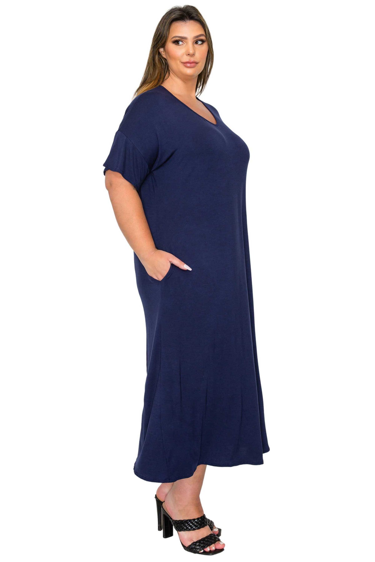 A woman modeling a navy blue short-sleeve maxi dress with a V-neckline and side pockets, paired with black heeled sandals, against a plain white background.