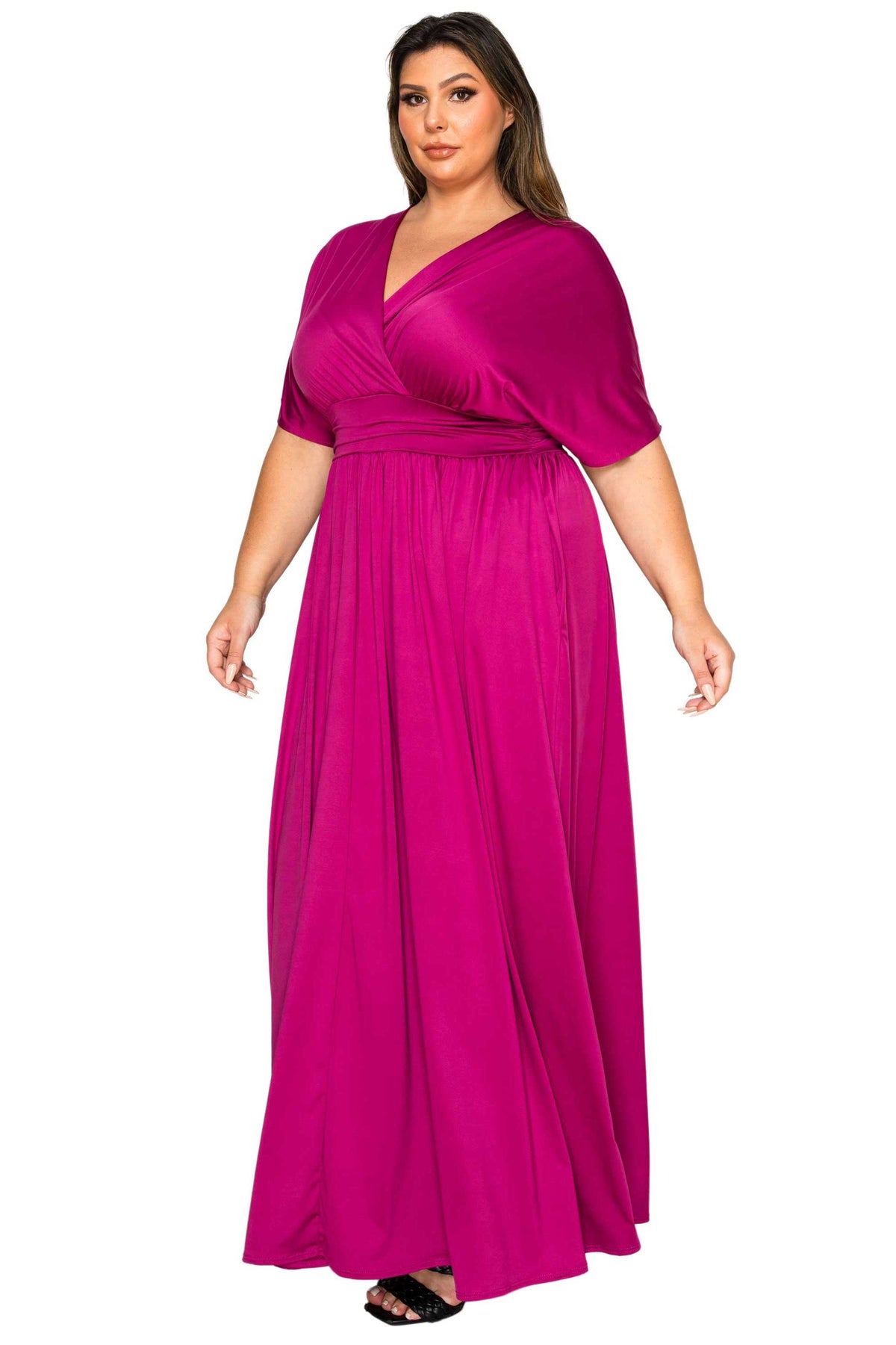 A woman modeling a magenta maxi dress with a wrap-style V-neck bodice, short sleeves, and a flowing skirt against a plain white background.