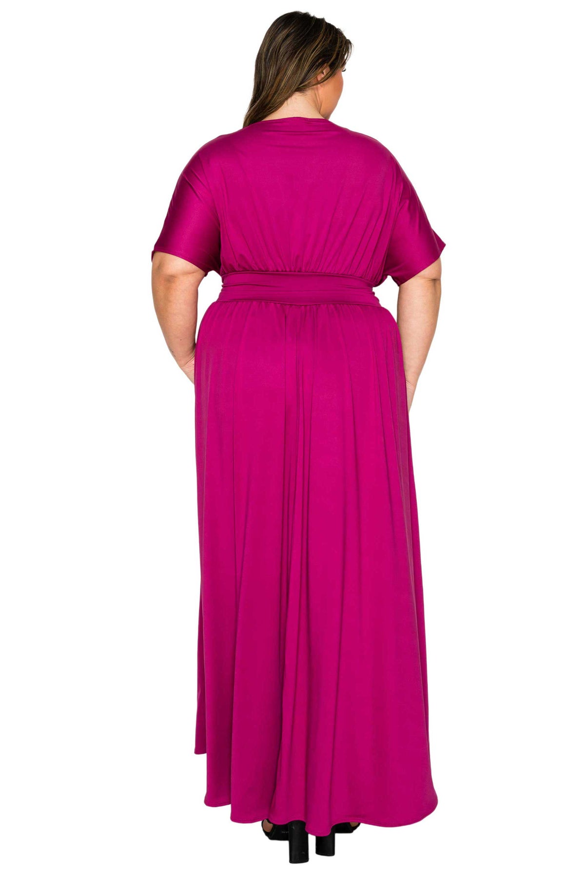A woman viewed from the back wearing a bright fuchsia magenta maxi dress with short sleeves and a matching waist tie, set against a plain white background.