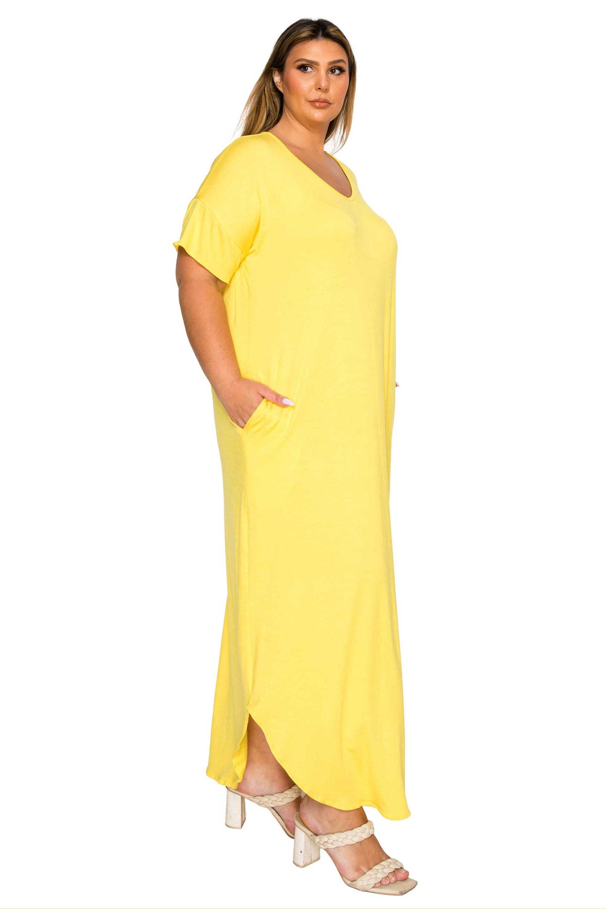 A woman modeling a bright yellow short-sleeve maxi dress with a V-neckline and side pockets, paired with beige high-heeled sandals, set against a plain white background.