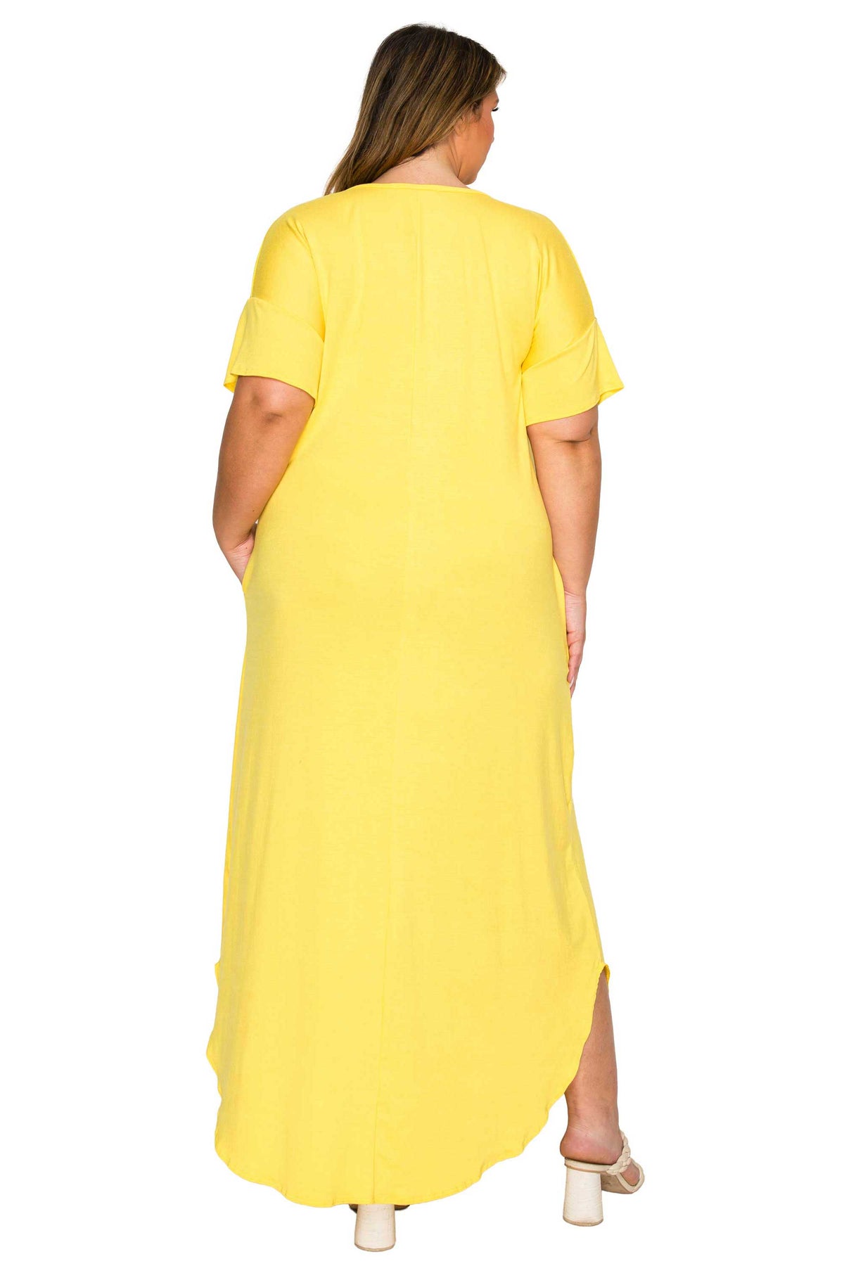 A woman viewed from the back wearing a bright yellow short-sleeve maxi dress with side pockets, paired with white block-heel sandals, against a plain white background.