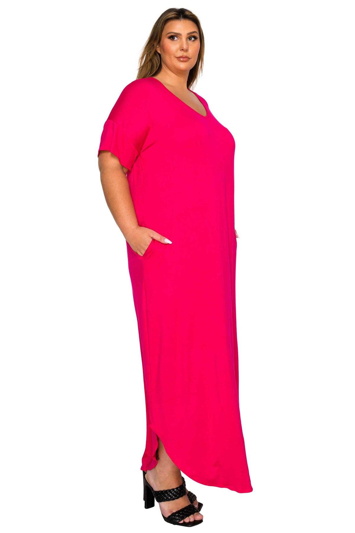 A woman modeling a bright hot pink maxi dress with short sleeves, a V-neckline, and side pockets, paired with black heeled sandals against a plain white background.