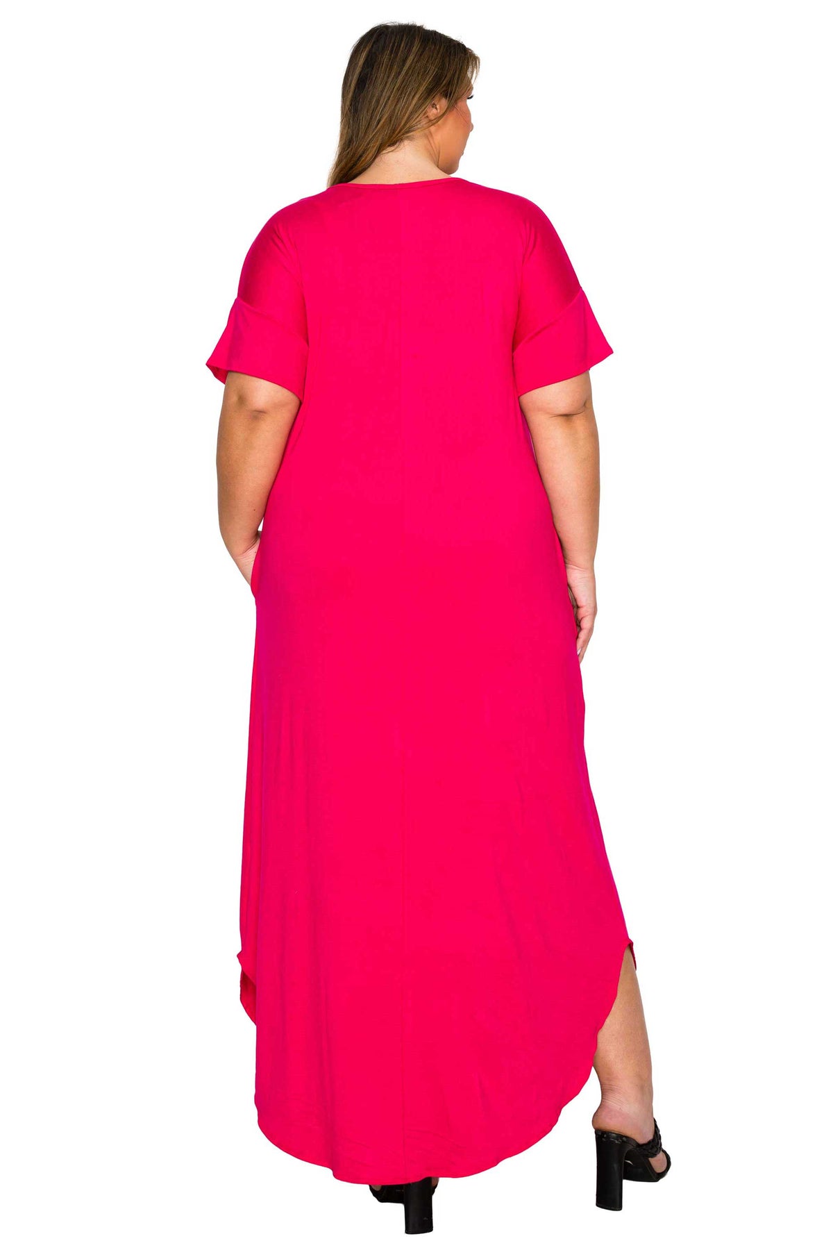 A woman viewed from the back wearing a bright hot pink short-sleeve maxi dress with a high-low hem and black heels, set against a plain white background.