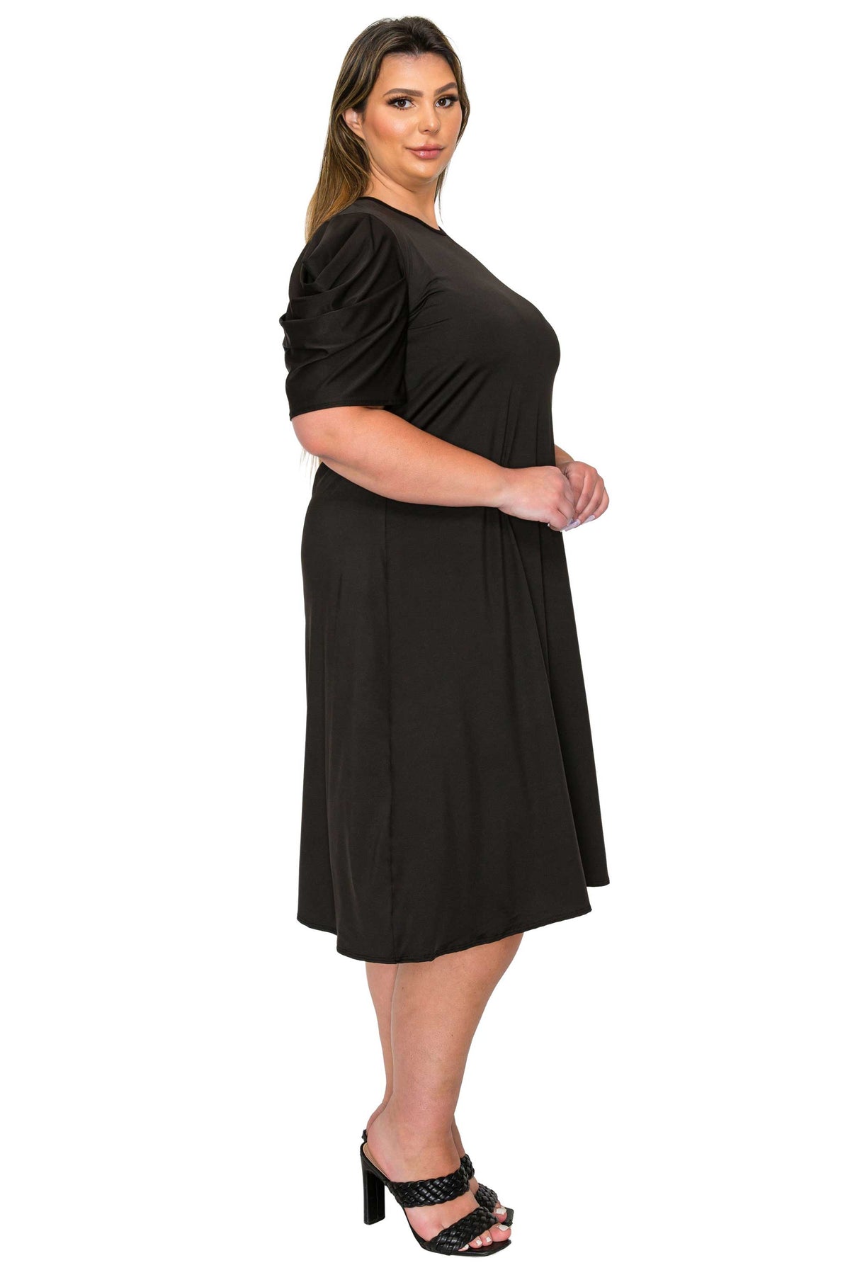 A woman modeling a black short-sleeve midi dress with puff sleeves and a flared skirt, paired with black heeled sandals, against a plain white background.