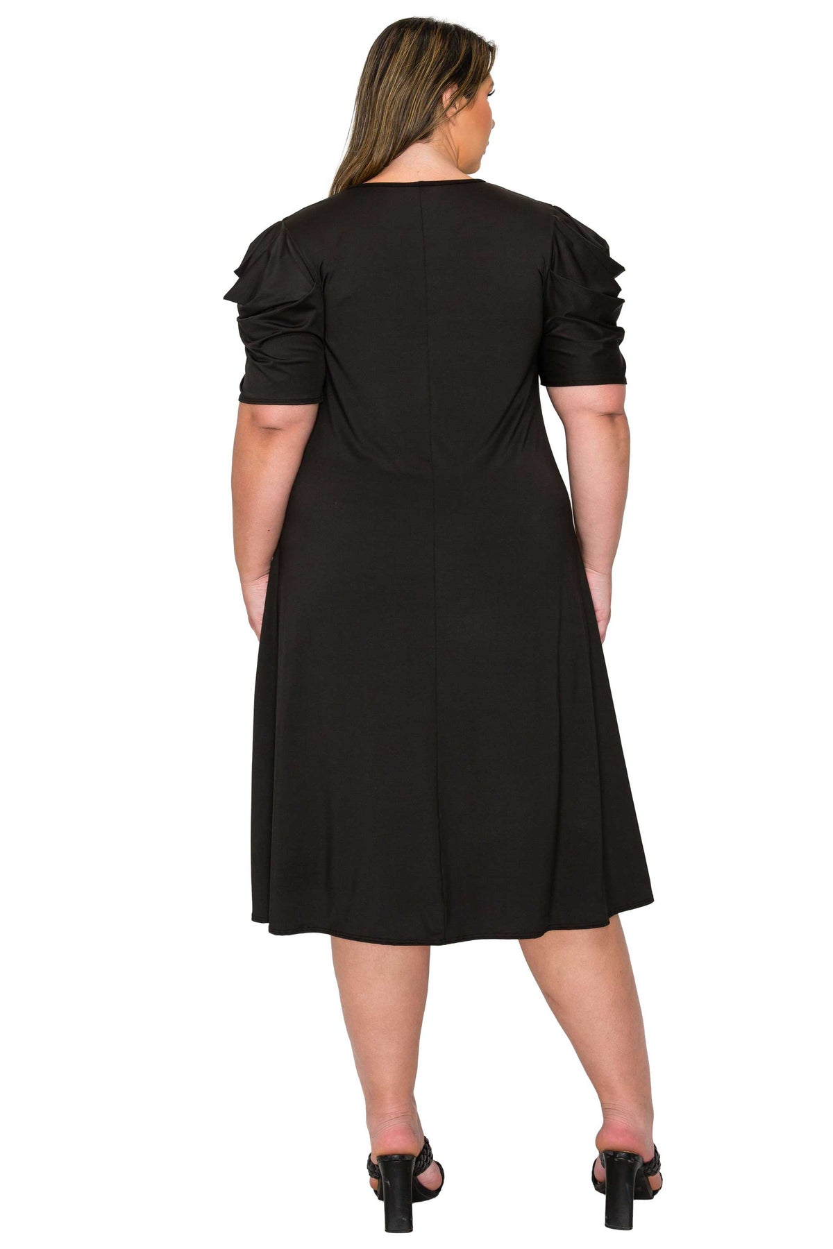 A woman viewed from the back wearing a black midi dress with short ruffled sleeves and a flared skirt, paired with black heeled sandals, against a plain white background.