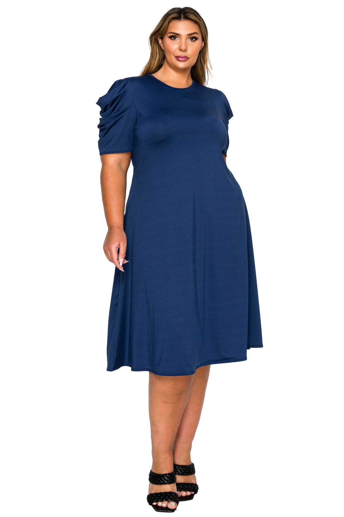 A woman modeling a navy blue midi dress with short ruffled sleeves and a flared skirt, paired with black strappy heels, against a plain white background.