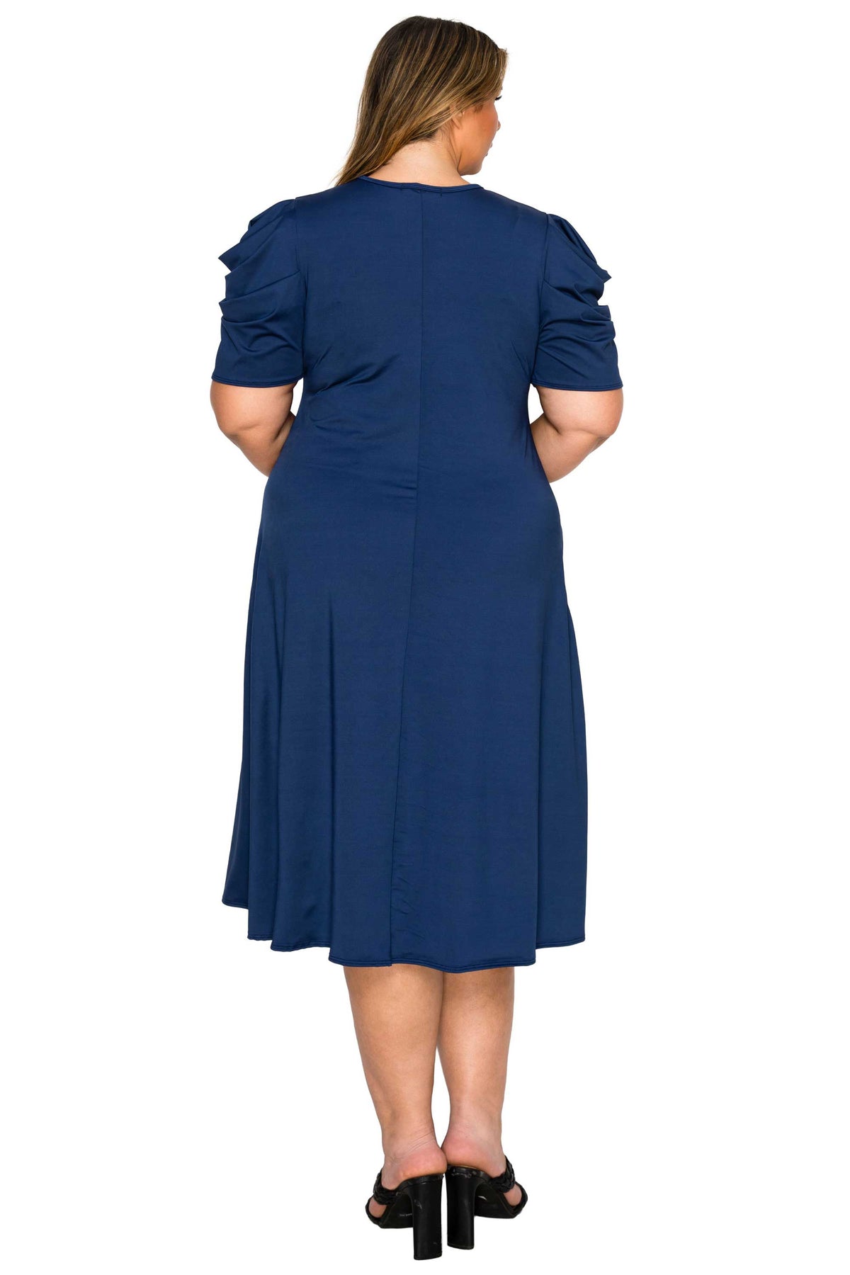 A woman viewed from the back wearing a navy blue knee-length dress with short ruffled sleeves and black heeled sandals, against a plain white background.