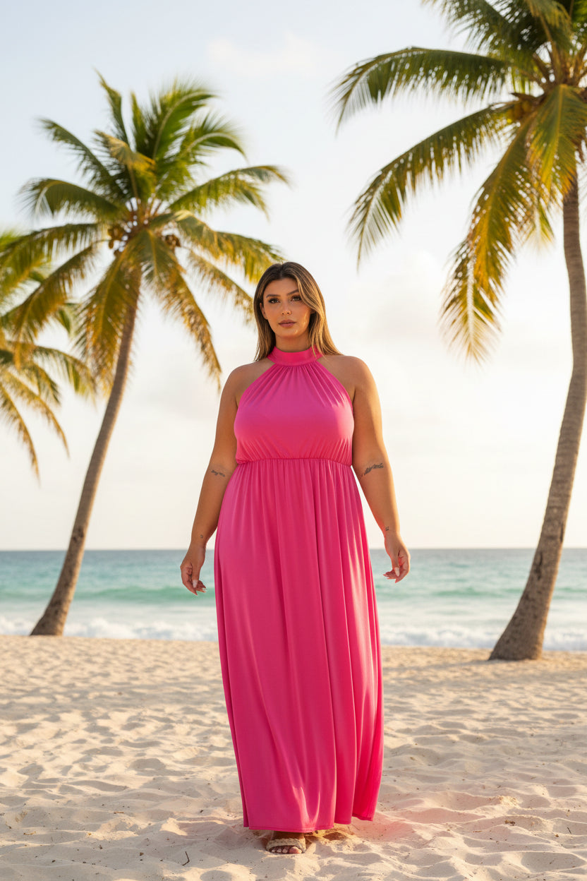 A woman modeling a bright pink halter-neck maxi dress with a flowing skirt, paired with beige heeled sandals, against a plain white background.