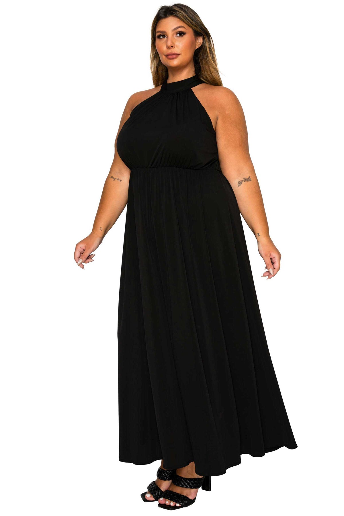 A woman modeling a black halter-neck maxi dress with a flowing skirt, paired with black strappy heels, against a plain white background.