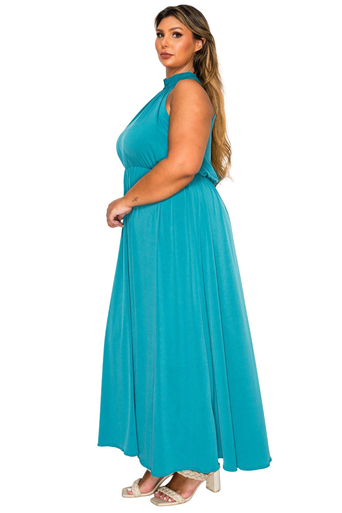 A woman modeling a sleeveless, high-neck, floor-length teal maxi dress against a plain white background.